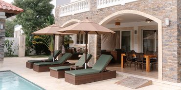 Poolside lounge chairs with umbrellas next to a stone-arched patio.
