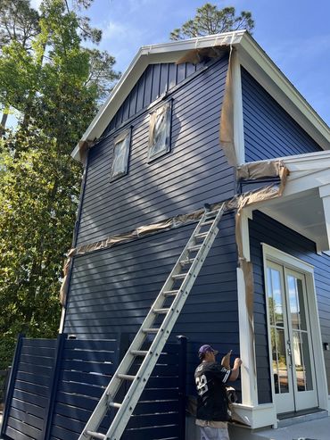 Painter masking trim while painting a two-story home navy blue
