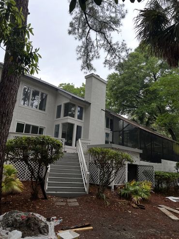 Back of a two-story white stucco home with a chimney during exterior work