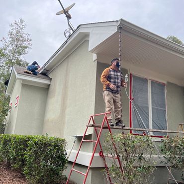 Painter on a ladder spray painting the stucco exterior of a home