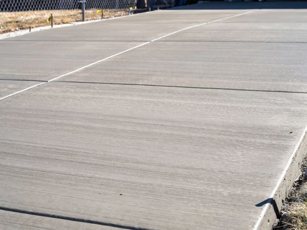 Newly laid concrete pavement with clean joints and a chain-link fence in the background.