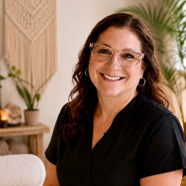 Smiling woman with glasses and hoop earrings in a cozy room.