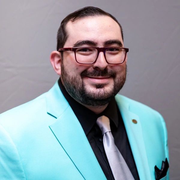 Man smiling in a turquoise blazer and glasses.