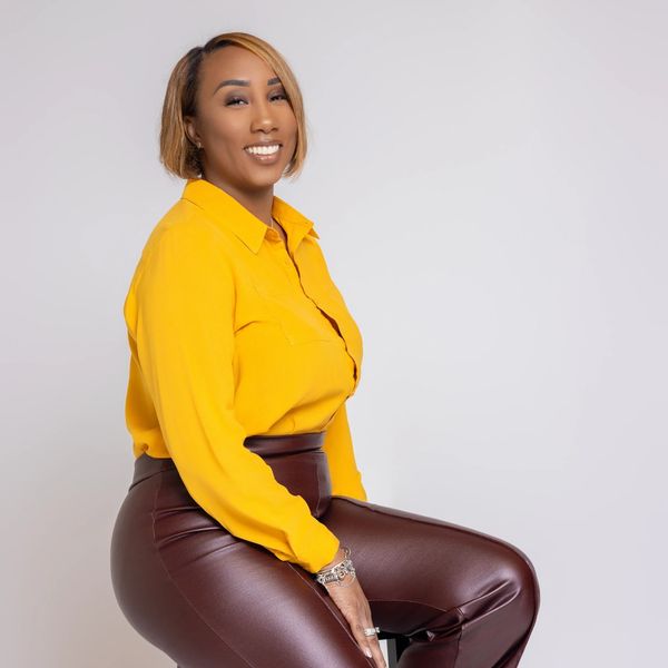 Woman smiling, wearing a yellow blouse and maroon pants.