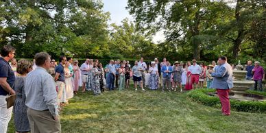 A man addressing a group of people outdoors in a garden setting.