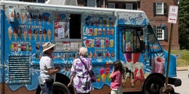 People ordering from a colorful ice cream truck on a sunny day.