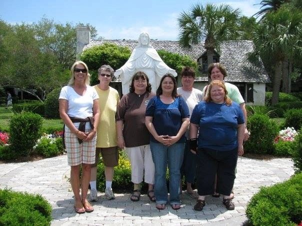 Group of six women posing in front of a statue and garden.