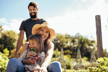 Happy family enjoying a sunny day in the garden with fresh vegetables.
