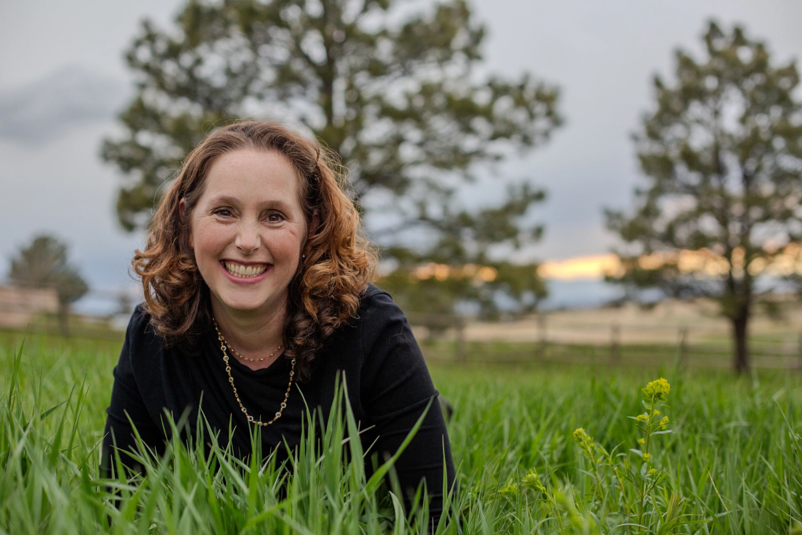 Smiling woman with curly hair lying in green grass outdoors.