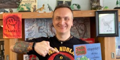 Man smiling and giving a thumbs-up in a colorful setting.