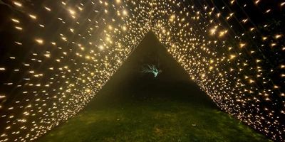 A triangular tunnel of warm white fairy lights at night.