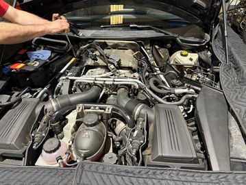 Open car engine bay with visible components and a person's hand.