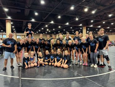 A large group of young athletes and coaches posing together indoors on a wrestling mat.