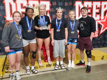 A group of young athletes wearing crowns and medals, posing happily at a wrestling event.