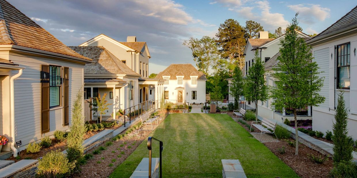 A serene neighborhood courtyard with white houses and green lawns at sunset.