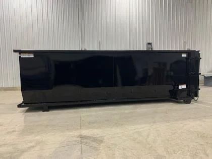 A large, black, rectangular industrial dumpster inside a warehouse.