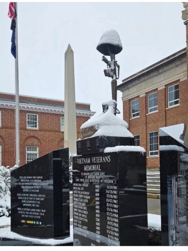 Snow-covered Vietnam Veterans Memorial with brick buildings in the background.