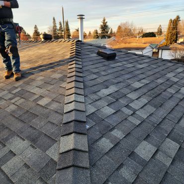 Rooftop with shingles and chimney with worker standing.
