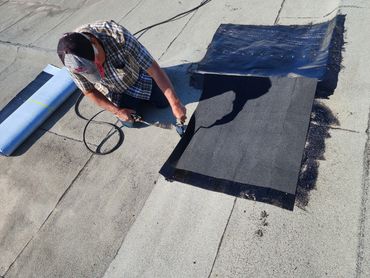 Man repairing roof with torch and roofing material.