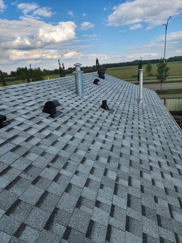 Shingled roof with multiple vents on a sunny day.