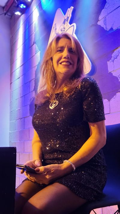 Woman in a sparkly black dress sitting with a phone under blue and purple lights.
