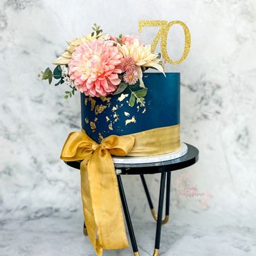 Navy blue cake with gold leaf, gold silk ribbon, 70 topper and floral arrangement 