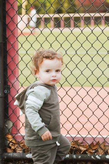 Toddler in green hoodie near chain-link fence.