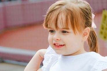 Smiling little girl with a ponytail and white dress.