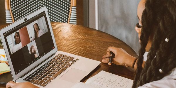 Woman attending an online video meeting while taking notes.