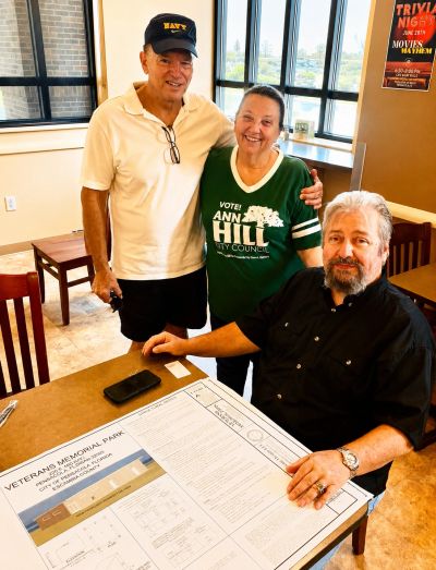 Ann Hill with Veterans Memorial Plaza board and plans for restroom on table