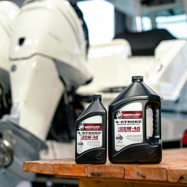 Two bottles of Mercury 4-stroke marine engine oil on a wooden table near boat engines.