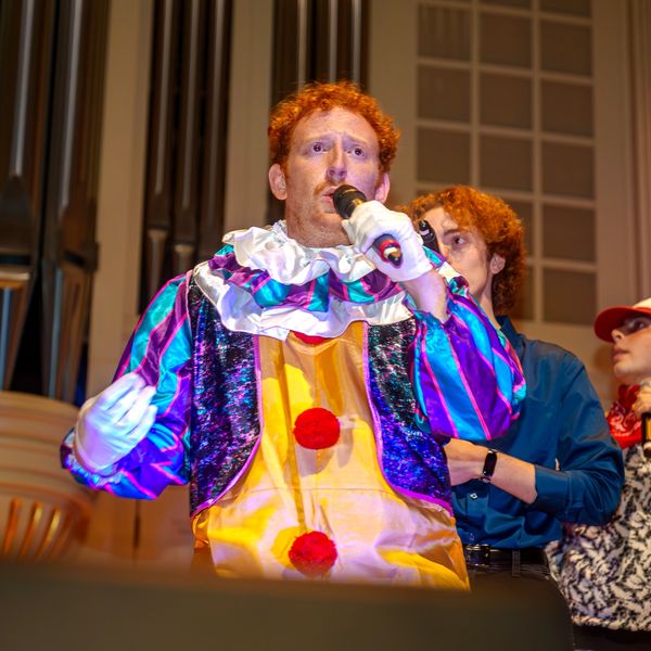 Man in colorful clown costume speaking into microphone.