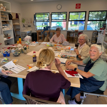 Four women happily crafting together around a large table in a bright room.