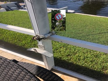 Close-up of a metal latch on a screened patio door with grass and water in the background.