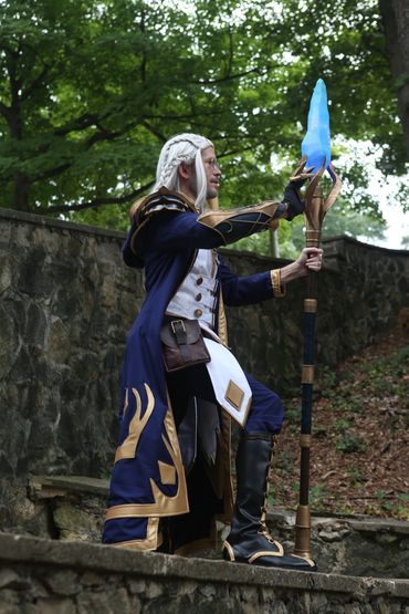 Person cosplay in fantasy wizard outfit holding glowing staff.