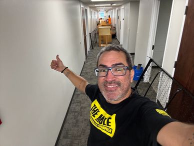 Man giving thumbs up in a hallway with furniture and items in the background.