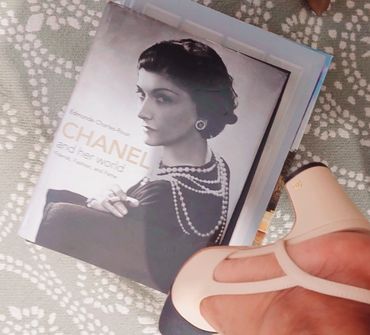 A vintage Chanel book and beige Chanel shoes on a patterned carpet.