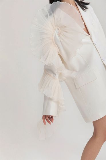 Elegant white blazer with dramatic ruffled sleeves worn by a model.