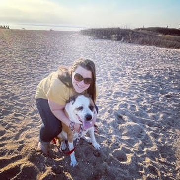 Woman hugging a happy dog on a sandy beach.