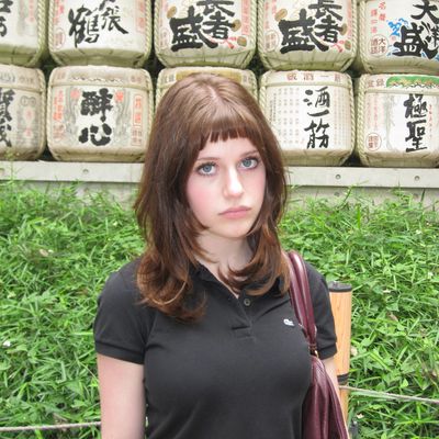 Young woman posing outdoors with traditional Japanese sake barrels in background.
