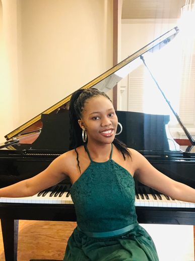 Young woman in green dress posing confidently by a grand piano.