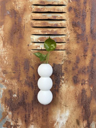 White stacked-ball Propagation Planter with a plastic test tube and green plant on rusty metal