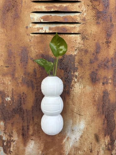 White stacked-ball Propagation Planter with a plastic test tube and green plant on a rusty vent wall