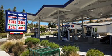 Front of a Rotten Robbie gas station with the price sign on the left, pumps under a canopy, and the 