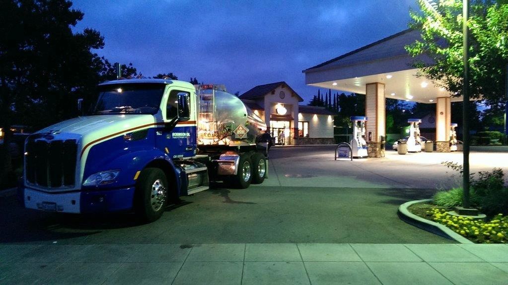 Rotten Robbie tanker truck at a gas station in the evening with dark sky.