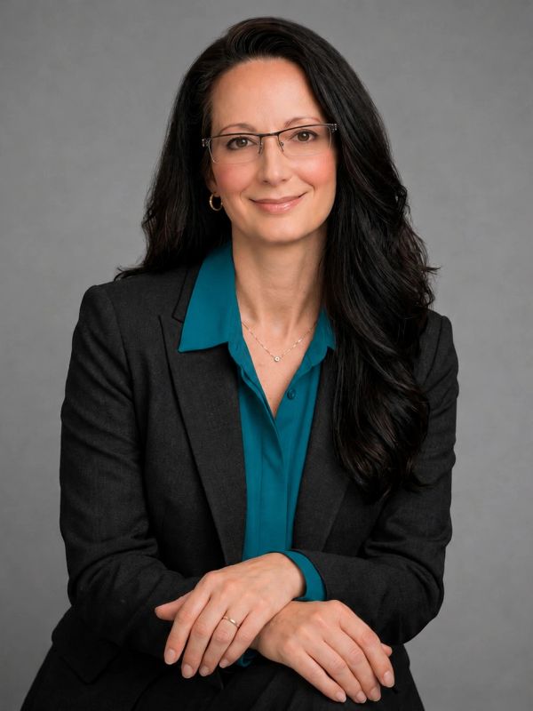 Professional woman in glasses and blazer smiling at the camera.