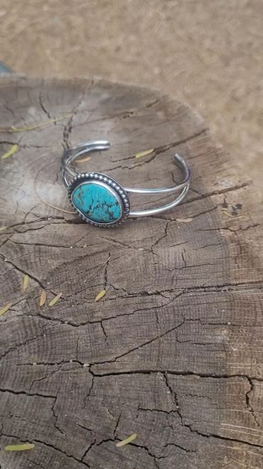 Silver bracelet with a turquoise stone on a cracked wooden surface.