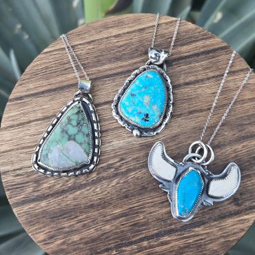 Three silver and turquoise stone necklaces on a wooden surface.