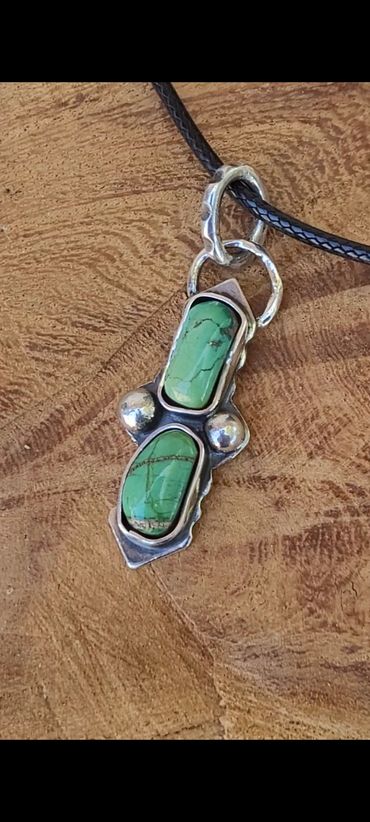 Silver pendant with two green stones on a black cord.