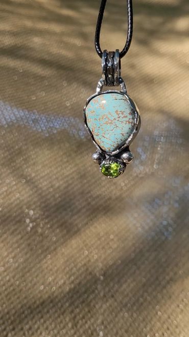 Close-up of a pendant with turquoise and green gemstone on a black cord.